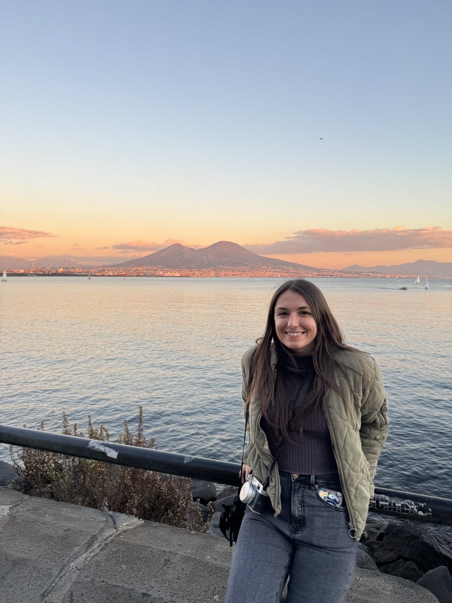 Audrey smiling by the water at sunset with Mount Vesuvius behind her
