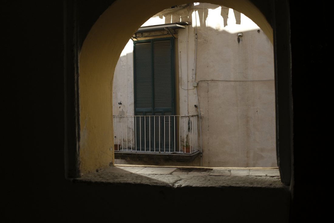 A view through a stone archway to a balcony with green shutters