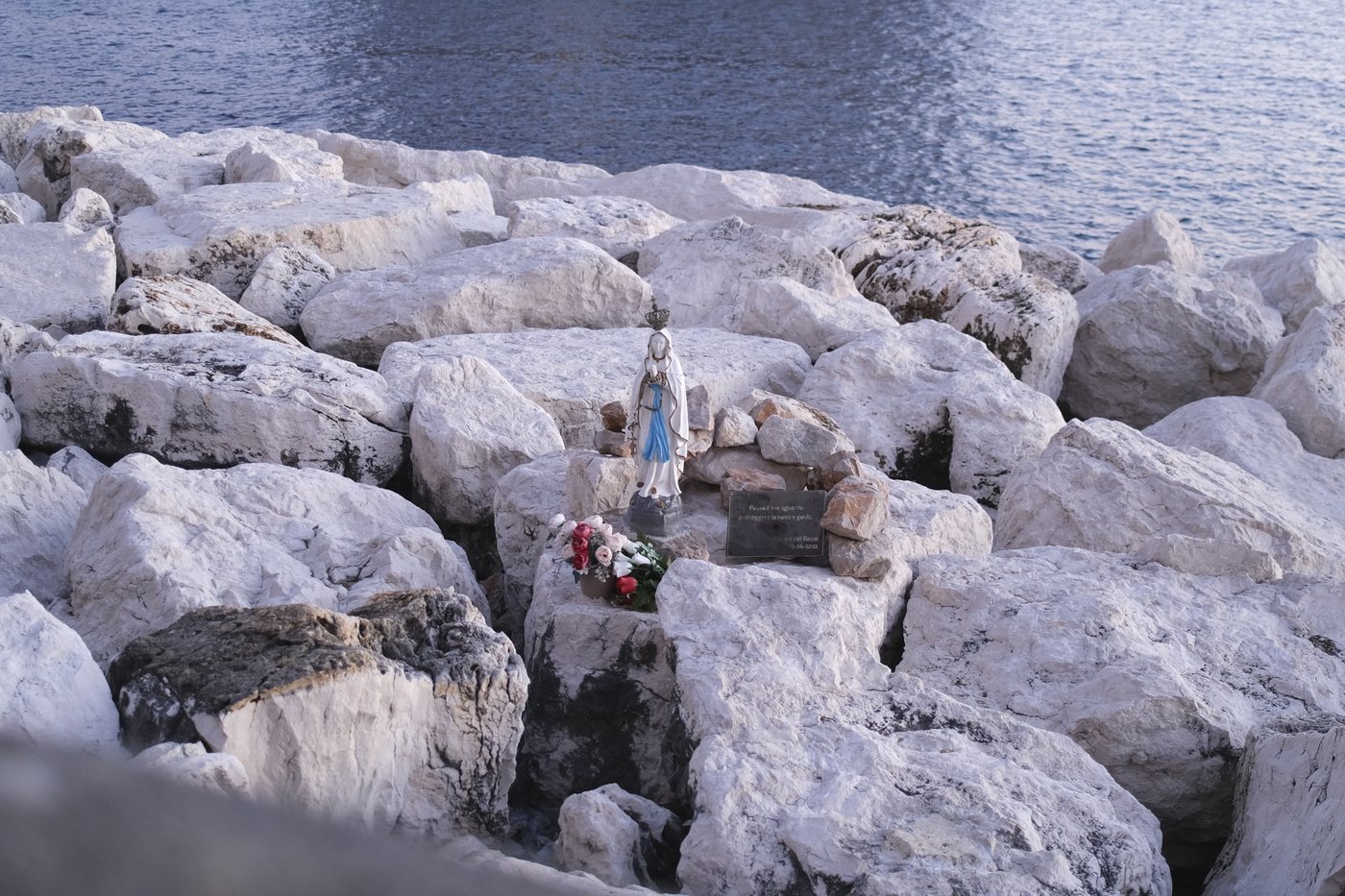 A statue of the Virgin Mary among white rocks on the shoreline