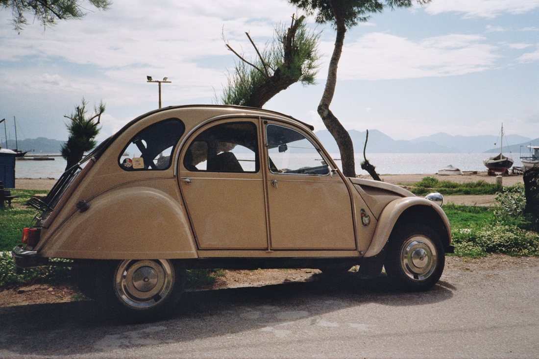 A vintage tan Citroën 2CV parked by the beach